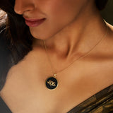A person wearing a gold pendant necklace with a black-and-white chevron pattern on a chain.