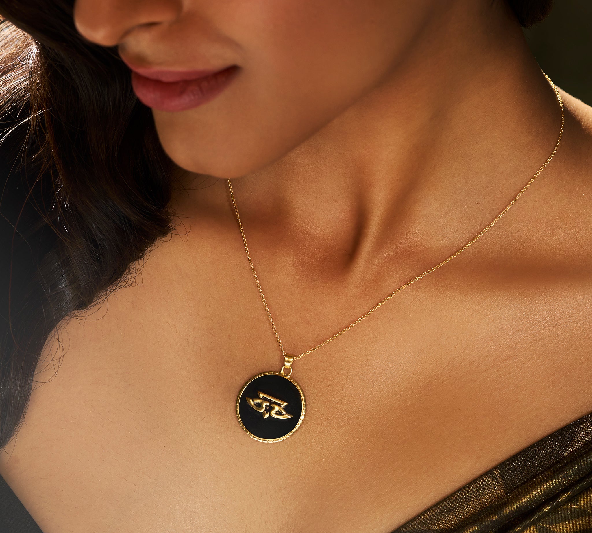 A person wearing a gold pendant necklace with a black-and-white chevron pattern on a chain.