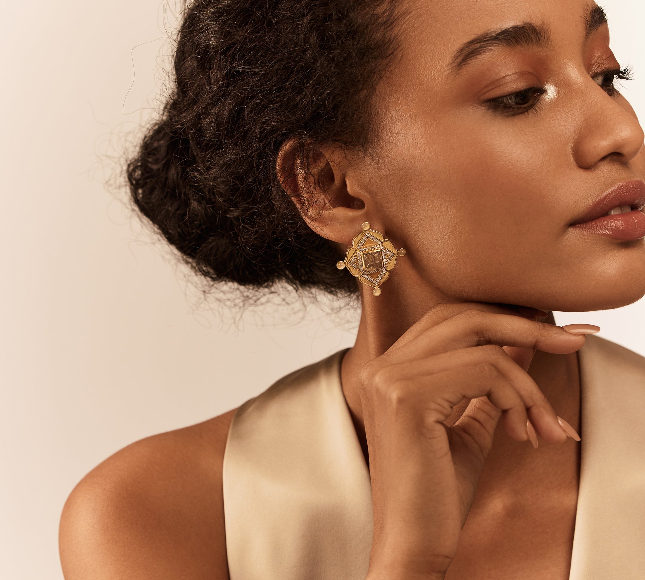 A person wearing a gold-colored earring with a geometric design and a semi-precious stone in the center.