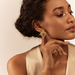 A person wearing a gold-colored earring with a geometric design and a semi-precious stone in the center.