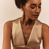 A person wearing a beige dress with a geometric design necklace featuring semi-precious stones and enamel work.