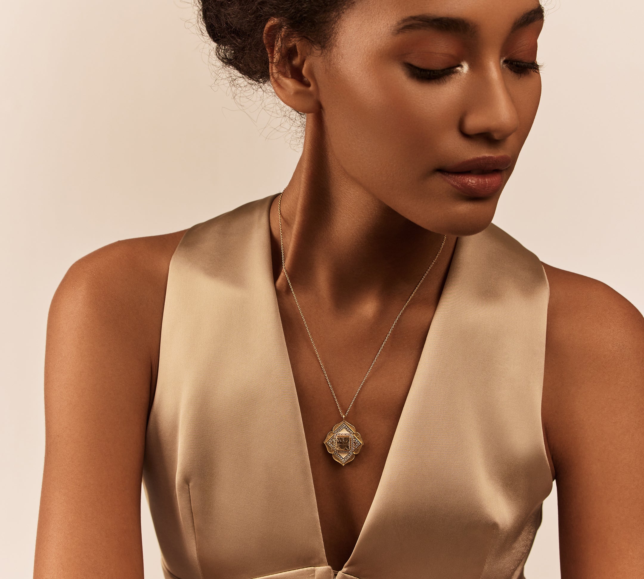 A person wearing a beige dress with a geometric design necklace featuring semi-precious stones and enamel work.