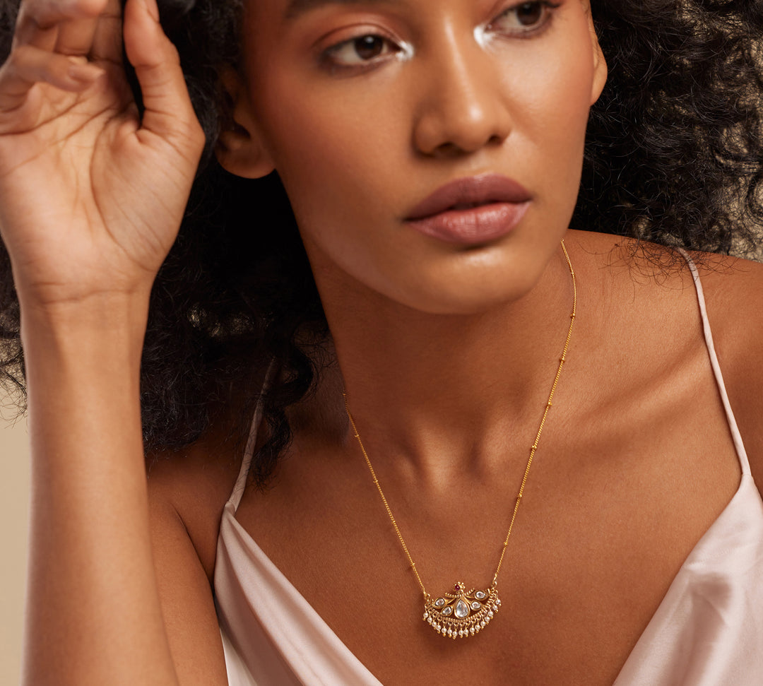 A woman wearing a semi-precious stone necklace with a gold chain and floral design pendant.