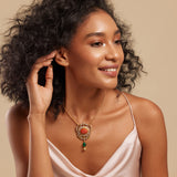A woman wearing a pink dress showcasing a gold necklace with a large orange semi-precious stone pendant and small green stone accents.