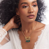 A woman wearing a white lace dress featuring a gold, enamel, and semi-precious stone necklace with a half-moon motif.