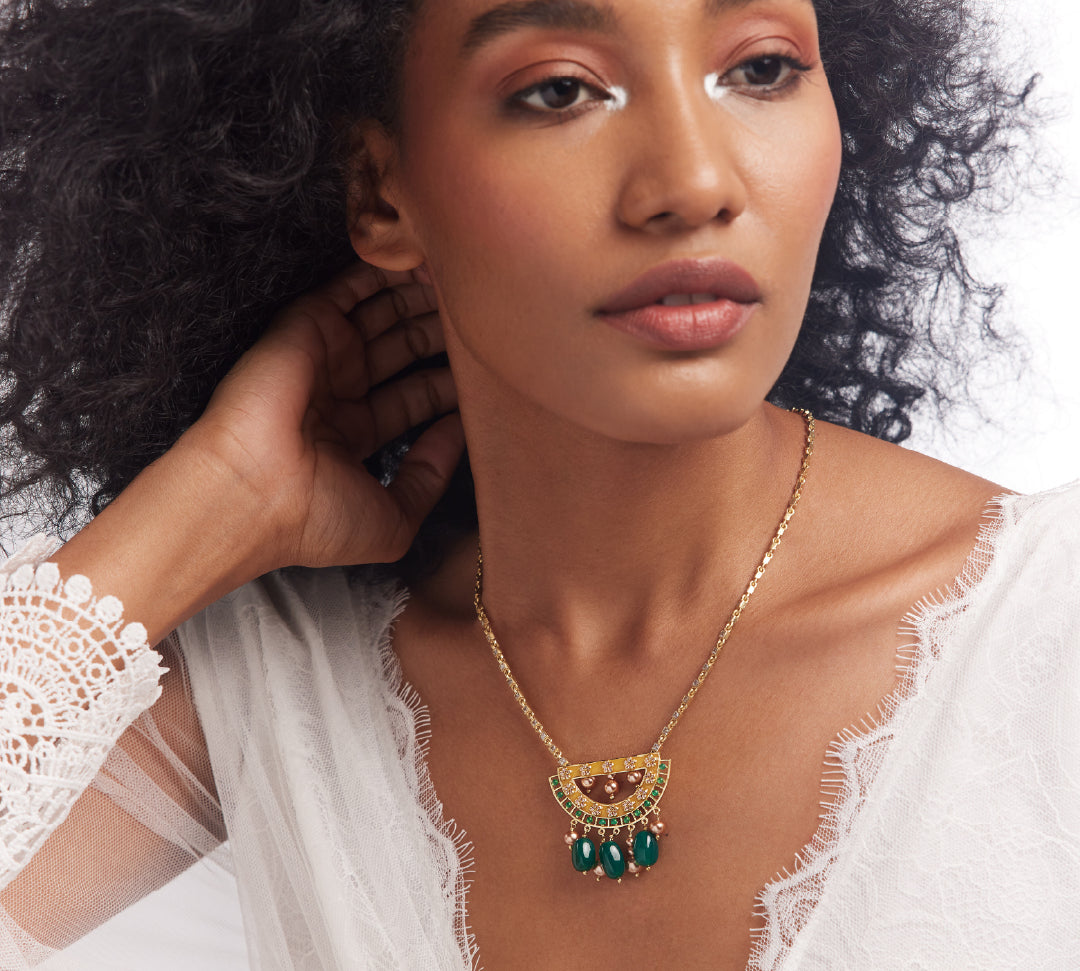 A woman wearing a white lace dress featuring a gold, enamel, and semi-precious stone necklace with a half-moon motif.