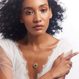 A person wearing a white outfit featuring a gold chainlet necklace with a geometric design, intricately carved semi-precious stones, and rich enamel work.