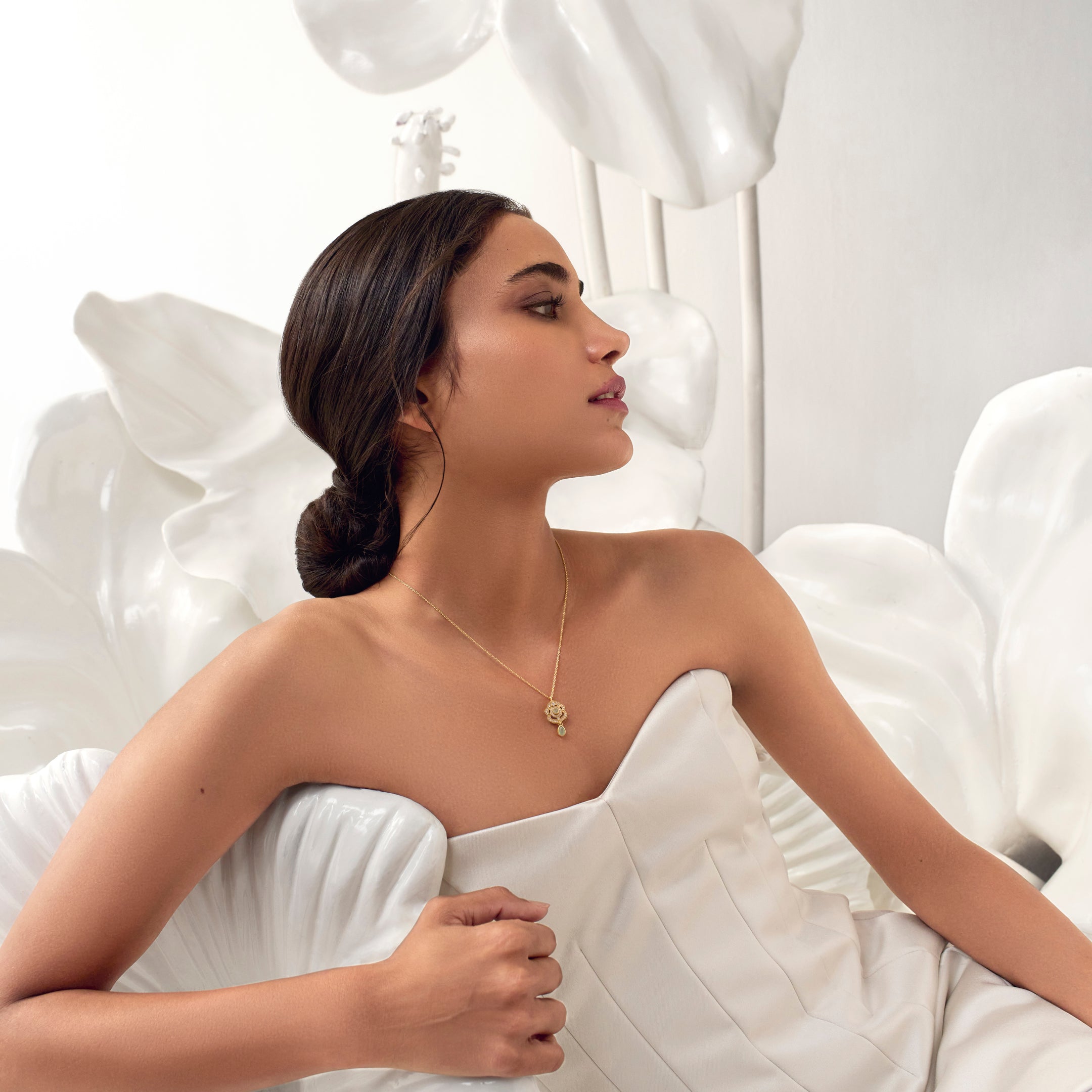 A woman wearing a white dress and a gold chainette pendant necklace with kundan stones.