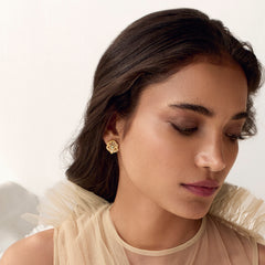 A person wearing a pair of dainty gold stud earrings adorned with zirconia-kundan stones.