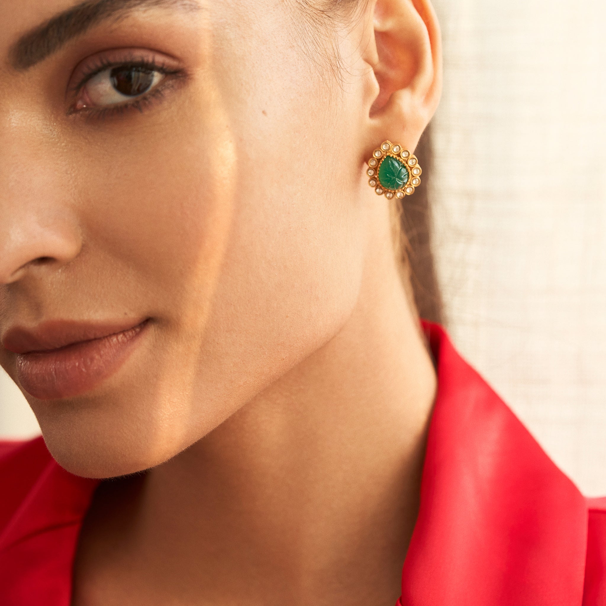 A close-up image of a woman's ear wearing a green emerald stud earring with gold detailing.